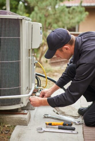 A technician from D and L Mechanical performs heat pump maintenance in Fredericksburg, VA, using tools and connecting refrigerant lines to an outdoor unit.