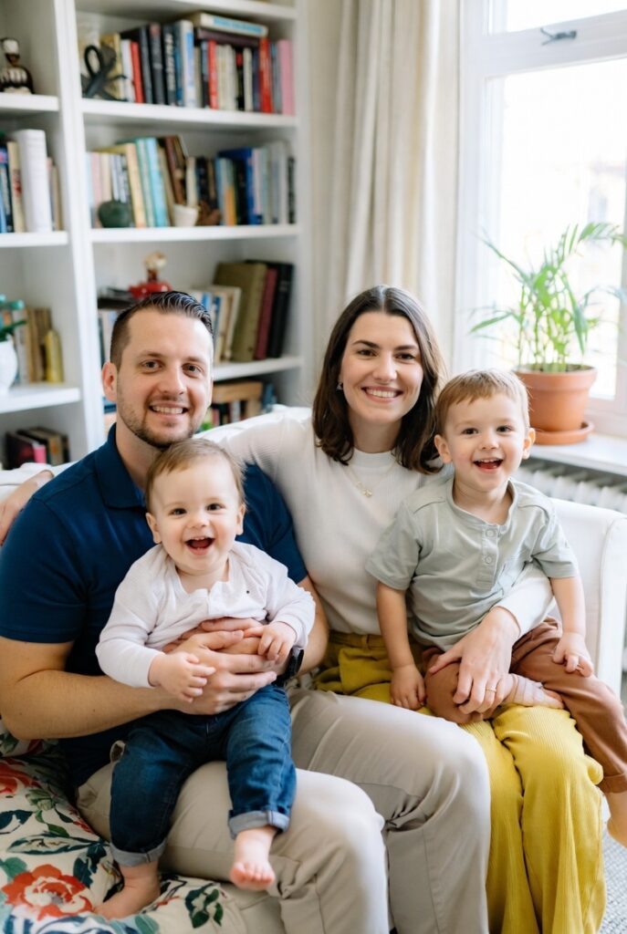 A smiling family of four relaxes comfortably on a couch in their cozy Fredericksburg, VA home, enjoying reliable indoor climate thanks to heat pump maintenance by D and L Mechanical.